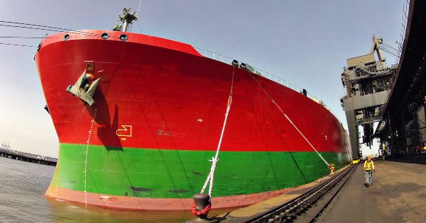 The bow of a large red and lime green ship at port, tethered by long lines.