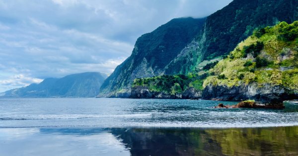 Scene from Madeira island. Steep, rocky cliffs and lush vegetation loom over peaceful ocean waters.