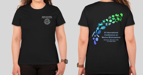 Black t-shirt, front and back, on a model. Front design: SSMB logo in white on the upper left chest. Back design: Silhouetted marine invertebrate larvae, colored in a bright gradient from indigo to lime green, arching over the conference name and dates in white text.